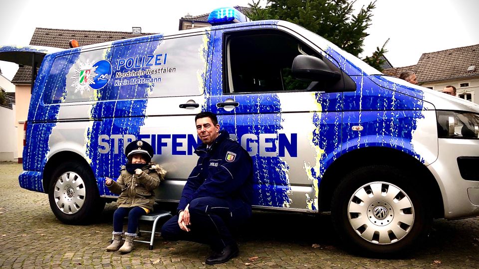 Bild zeigt den neuen Streifenwagen, einen Polizeibeamten und ein Kind