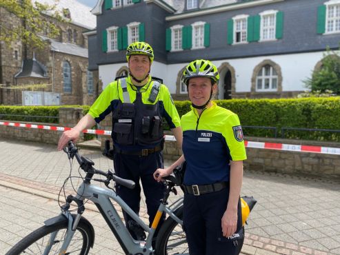 Eine Polizistin und ein Polizistin mit Helm posieren neben einem Fahrrad. 