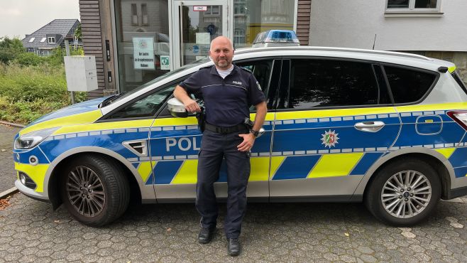 Der neue Bezirksdienstbeamte Tim Böger steht vor einem Streifenwagen an der Polizeiwache Heiligenhaus.